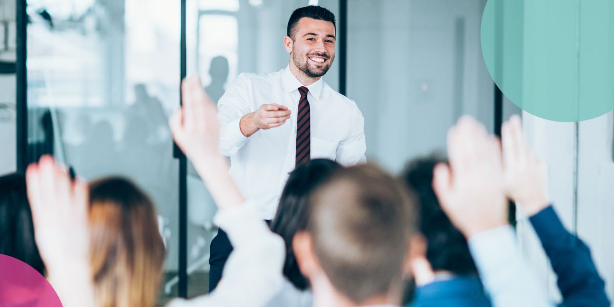 Business man standing at the front of a crowd in an office, looking out at raised hands