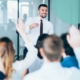 Man in an office facing a crowd with raised hands