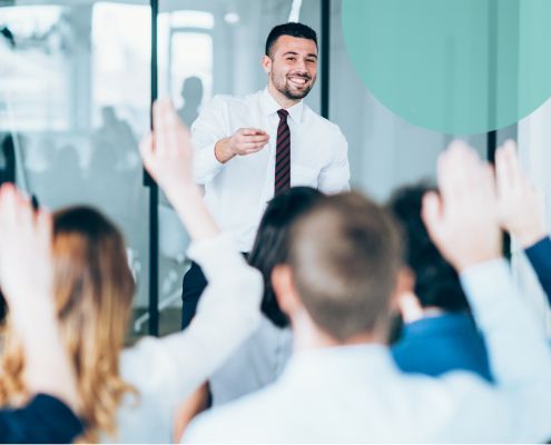 Man in an office facing a crowd with raised hands